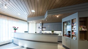Un área de recepción moderna con techo de madera, mostrador de recepción y una vitrina de vidrio con folletos.