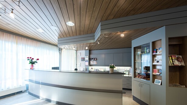 A modern reception area with a wooden ceiling, a reception desk, and a glass display case with brochures. - Hotel Waldhorn (Bern)