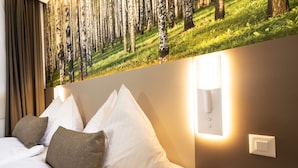 A hotel room with a bed, pillows, a wall-mounted light, and a forest-themed mural. - Hotel Waldhorn (Bern)