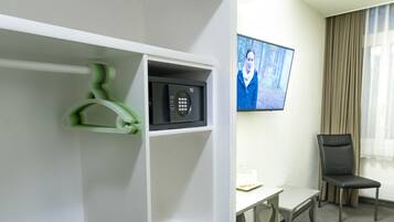 Una habitación de hotel con un armario blanco, un televisor de pantalla plana montado en la pared, un escritorio y una silla.