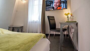 Habitación de hotel con cama, escritorio, silla, televisor en la pared y ventana con cortinas.