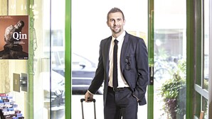 A man in a suit with a suitcase, standing in a hotel lobby with a glass door and a poster of a sculpture. - Hotel Waldhorn (Bern)
