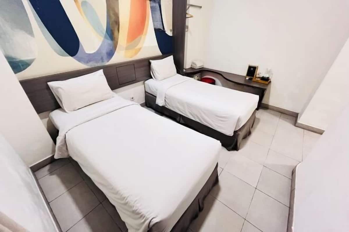 Habitación de hotel con dos camas, una mesita de noche, un cuadro en la pared y suelo de baldosas.