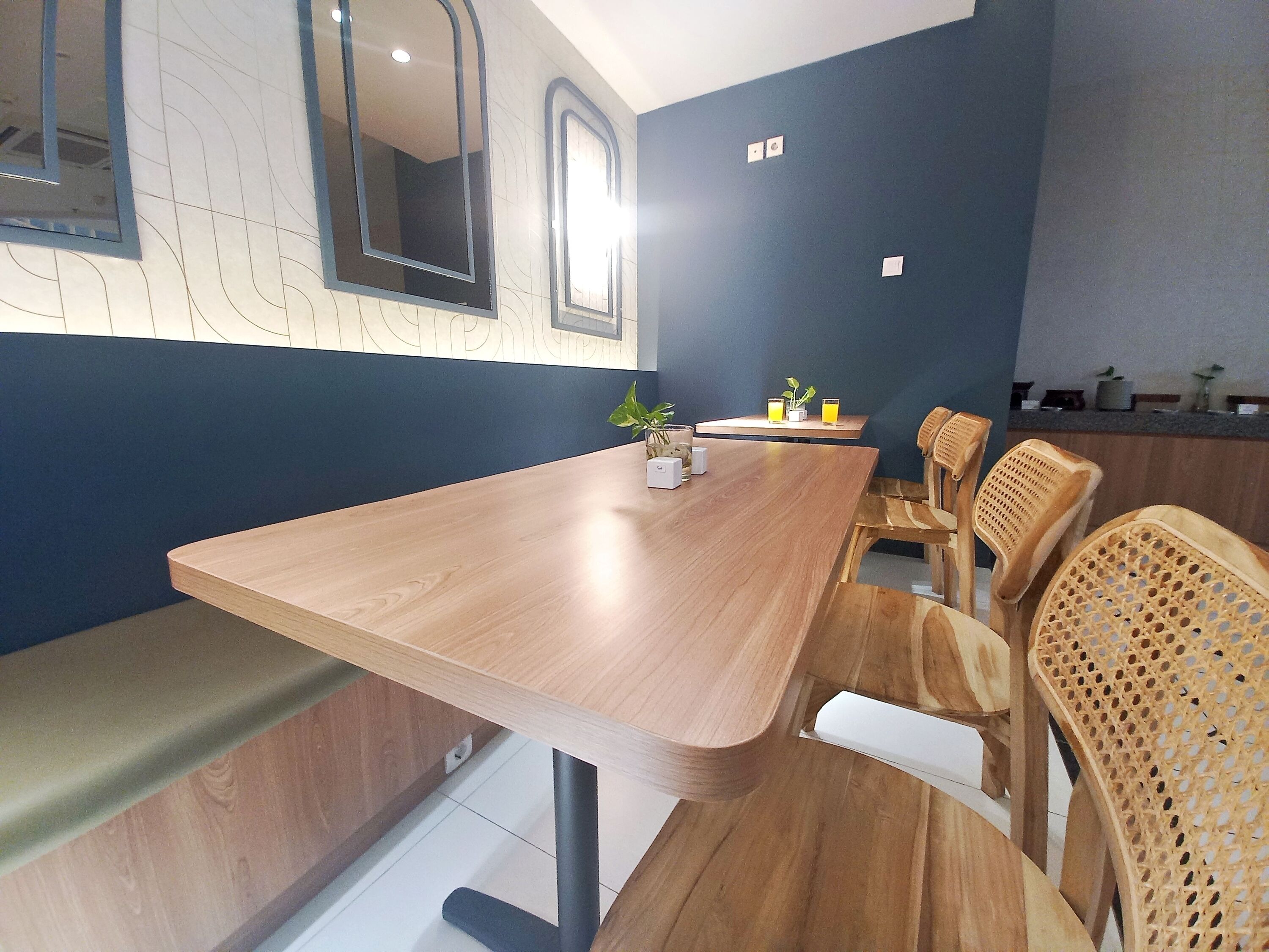 Una sala de conferencias moderna con una larga mesa de madera, bancos acolchados y sillas de mimbre.