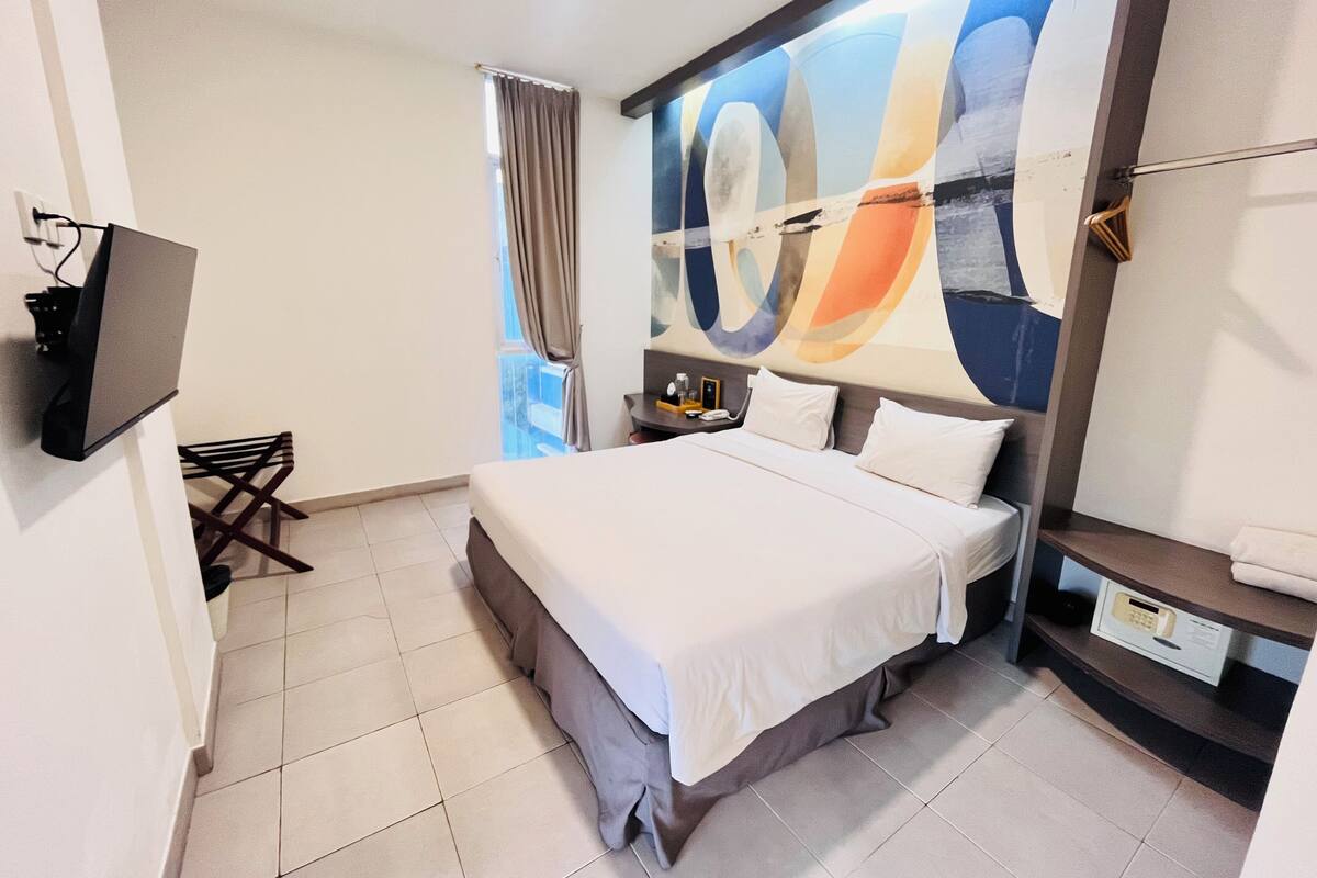 Una habitación de hotel moderna con una cama grande, un escritorio y un televisor instalado en la pared.