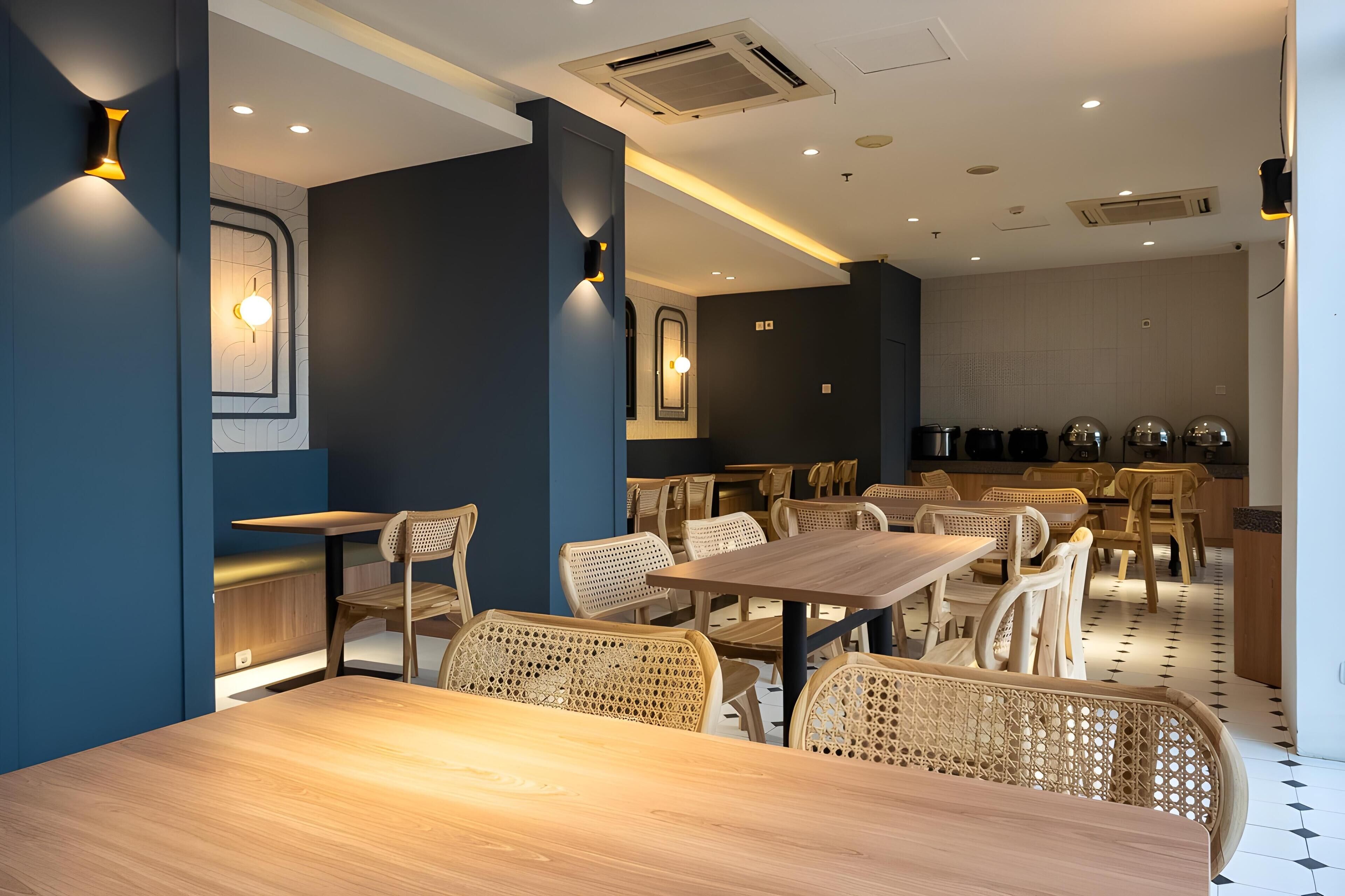 A modern restaurant with wooden tables and chairs, recessed ceiling lighting, and a kitchen area in the background.
