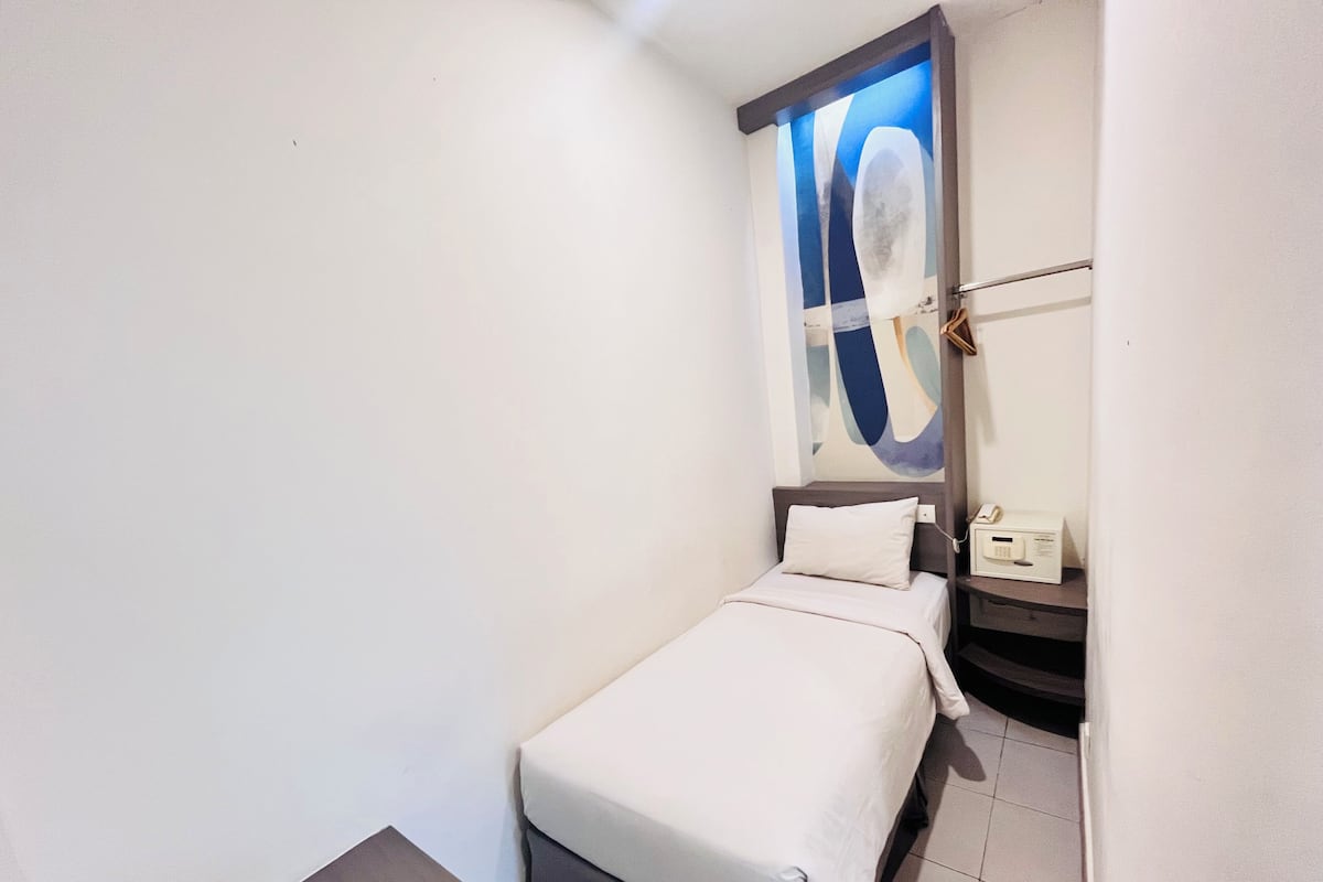 Un dormitorio pequeño y ordenado con una cama individual, una mesita de noche con lámpara y una obra de arte colgada en la pared.