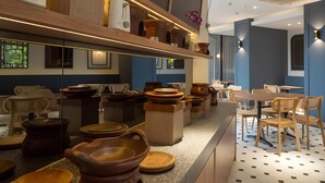 A restaurant interior with a long counter, wooden chairs, and terracotta pots displayed on shelves. - Hotel 88 Kedoya Jakarta (Jakarta)