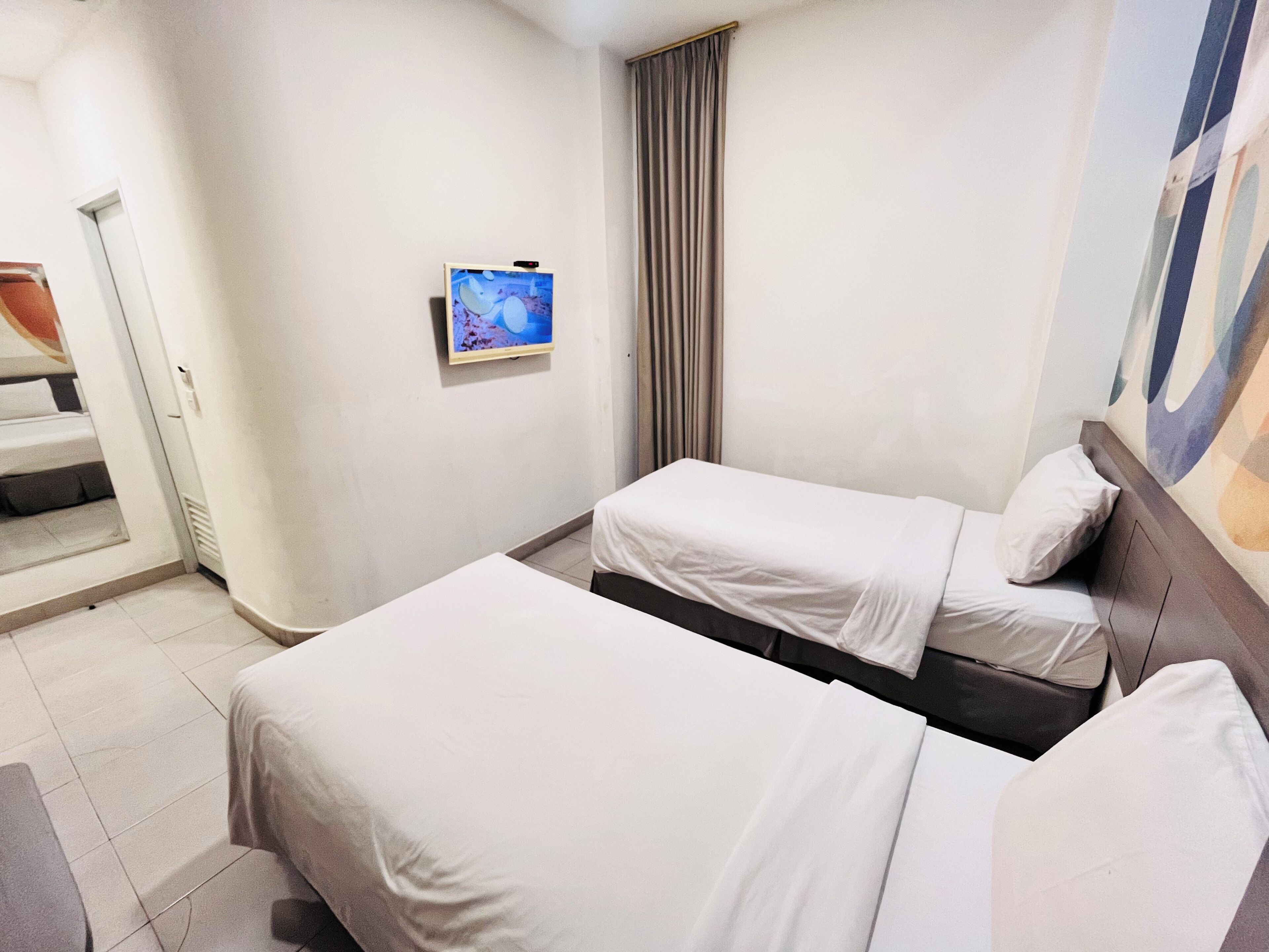 Ein Hotelzimmer mit zwei Betten, einem Wandfernseher und einem Fenster mit Vorhängen.