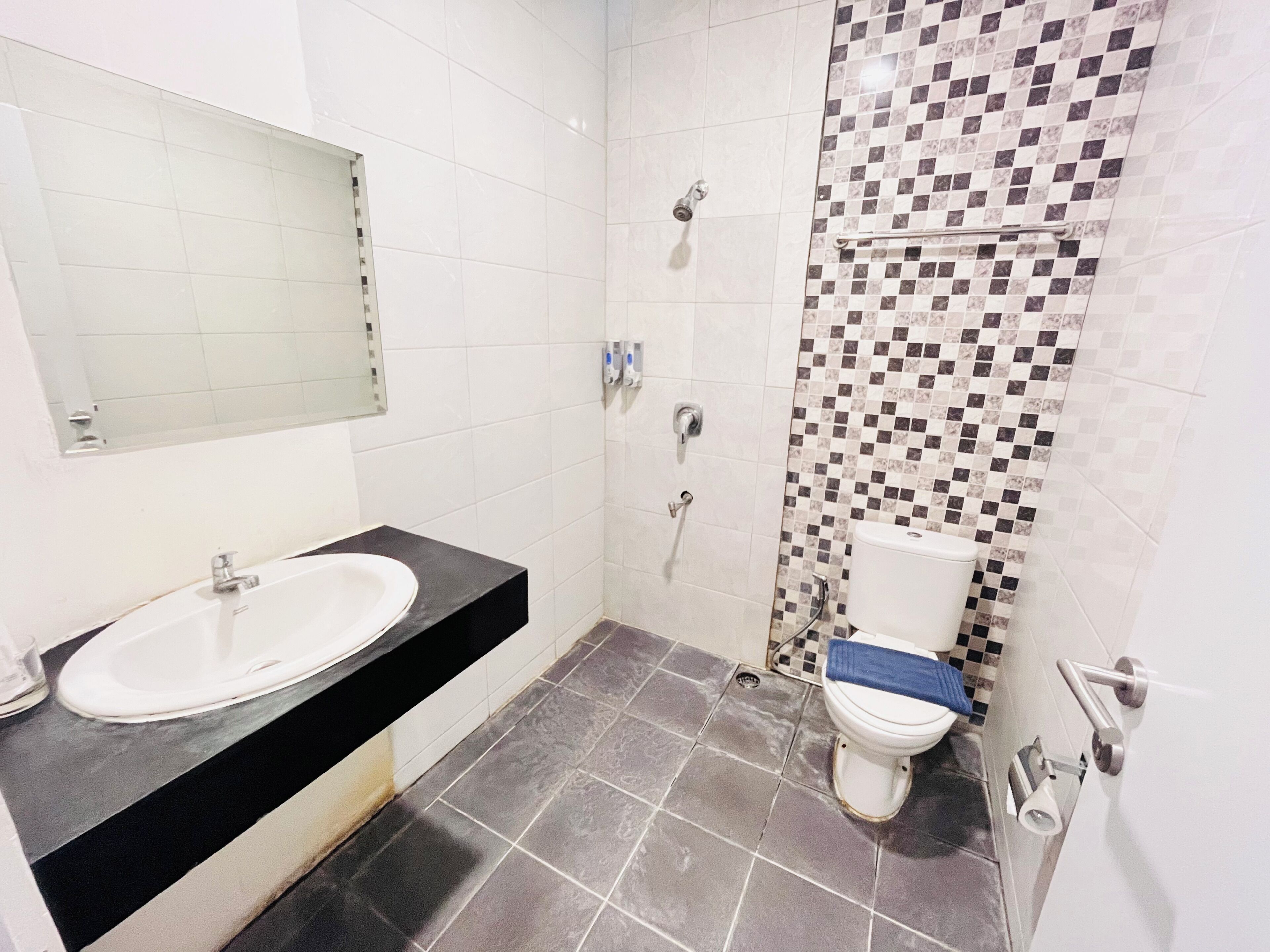 A bathroom with a white sink, black countertop, and a shower with a checkered tile wall.