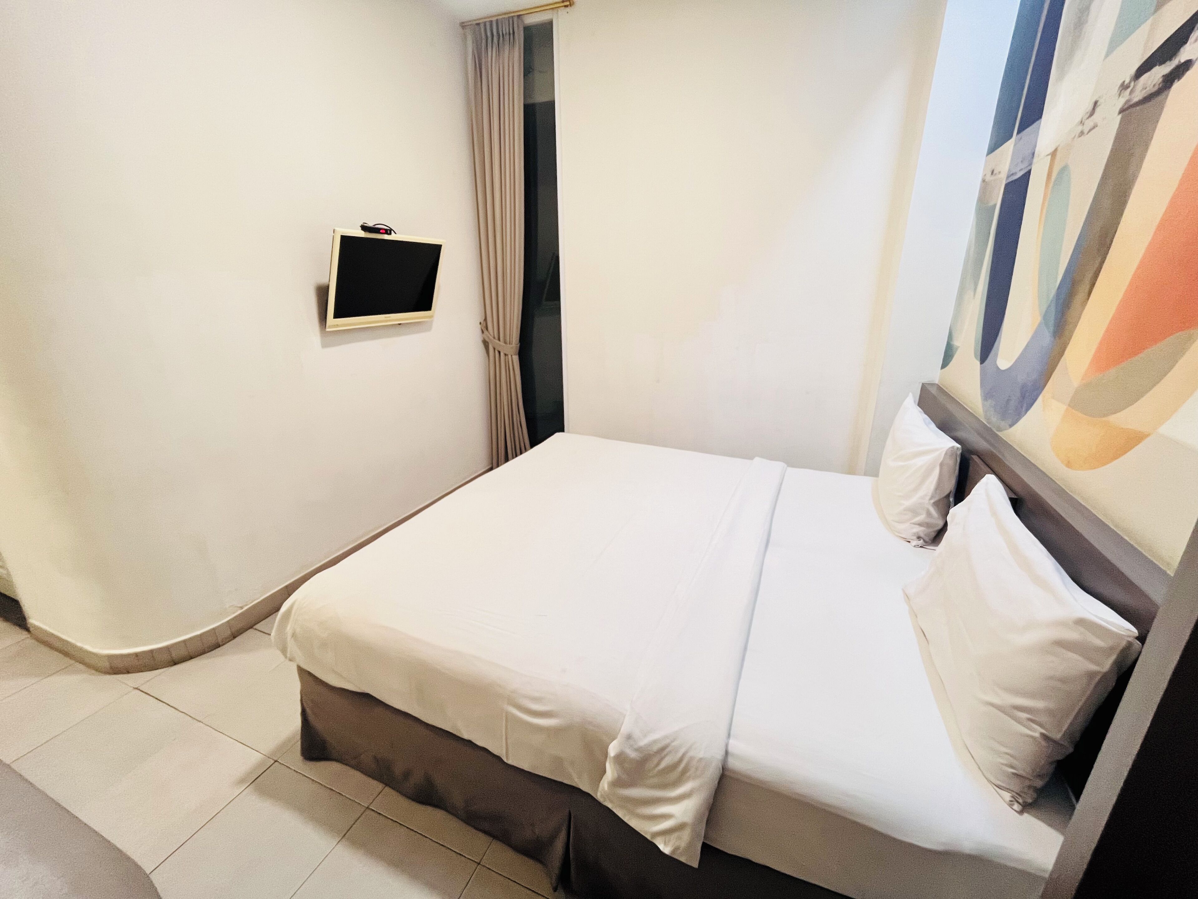 A neatly made bed with white bedding, a small bedside table, and a wall-mounted TV.