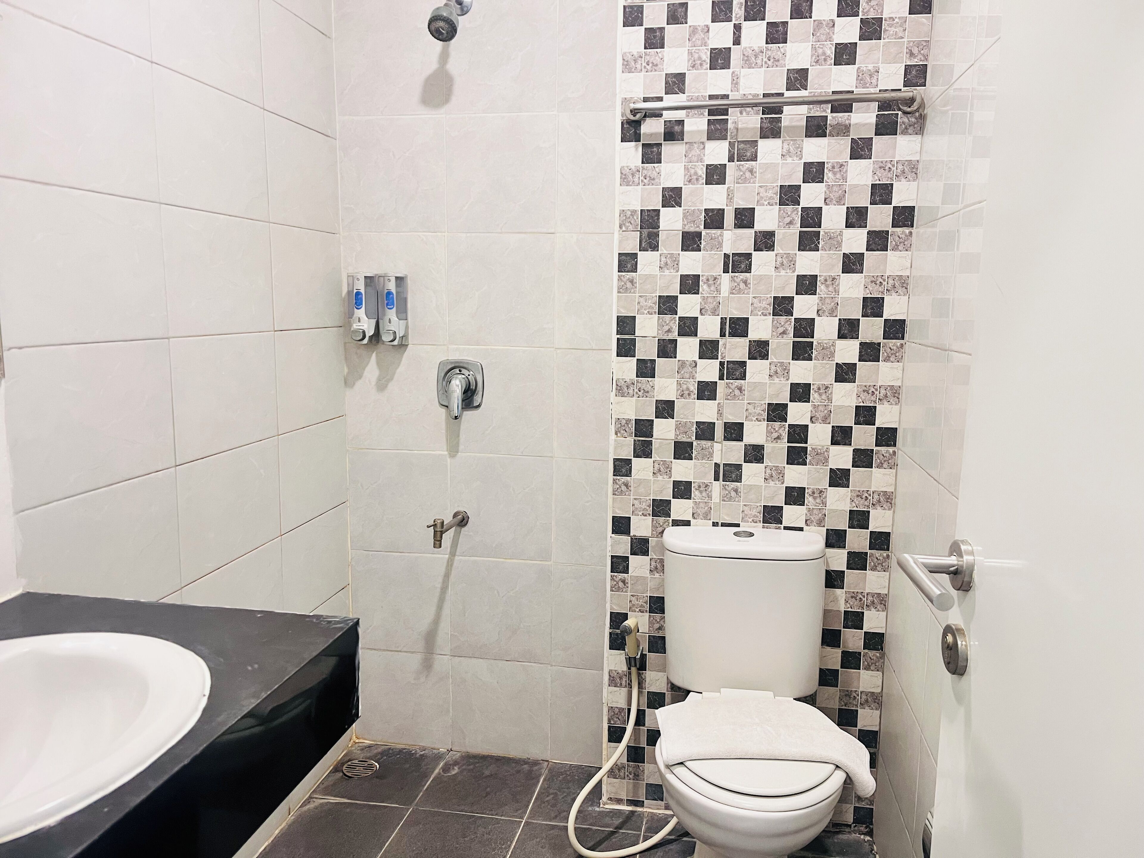 A bathroom with a white toilet, a shower with a checkered tile wall, and a black countertop with a sink.