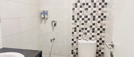 Une salle de bain avec des toilettes blanches, une douche dont le mur est recouvert de carreaux à motifs et un plan de toilette noir avec un lavabo.