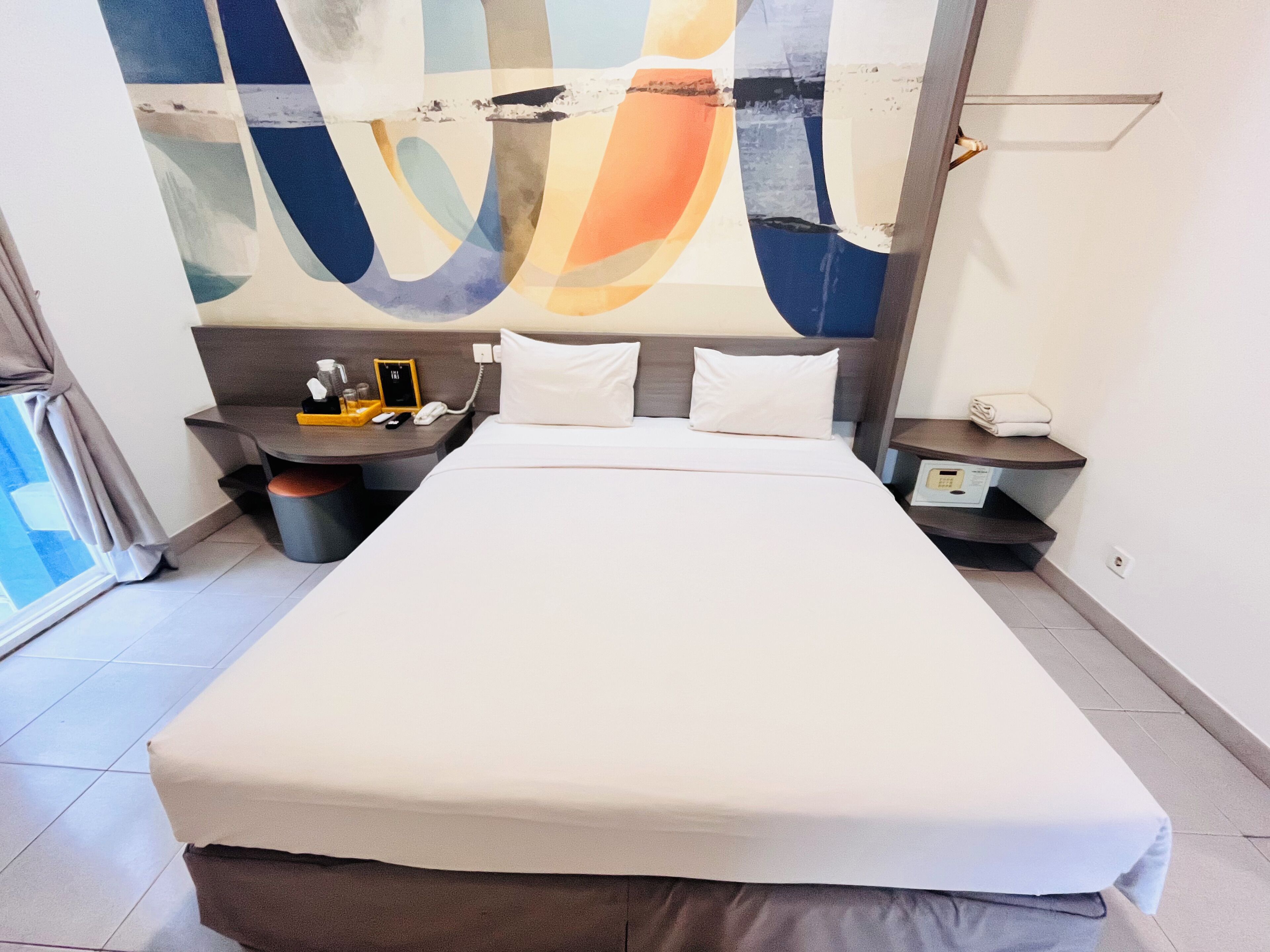 Een moderne hotelkamer met een groot bed, een nachtkastje, een wandtelefoon en een raam met uitzicht.