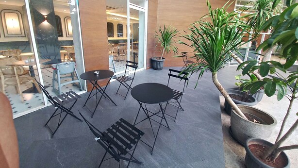 An outdoor seating area with tables and chairs, potted plants, and a view of the interior. - Hotel 88 Kedoya Jakarta (Jakarta)