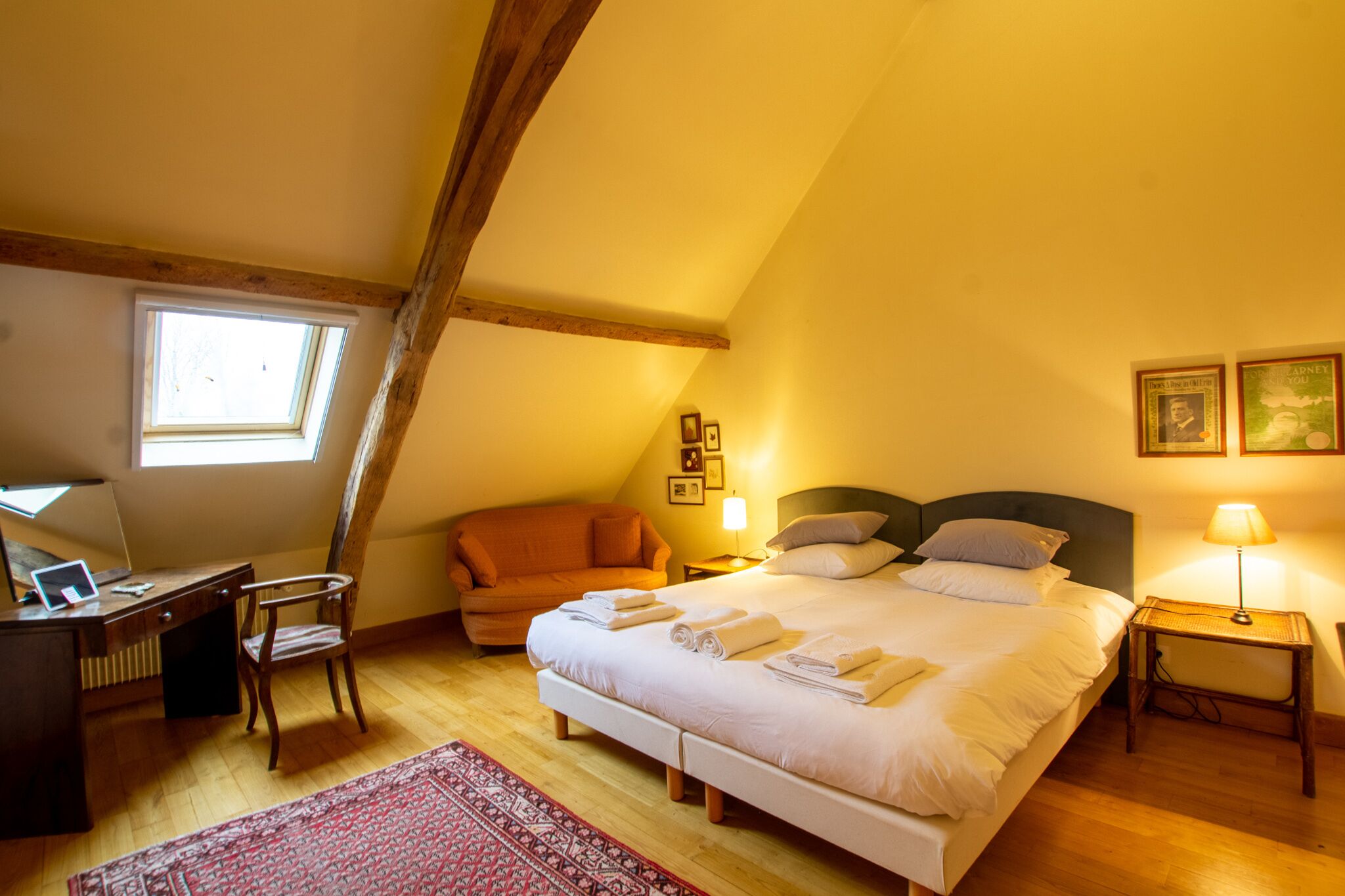 Ein gemütliches Schlafzimmer mit einem großen Bett, einem Schreibtisch und einem Stuhl, ausgestattet mit Holzbalken und einem Oberlicht.