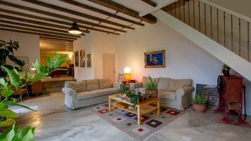 A living room with a sofa, coffee table, and potted plants. There is a staircase with a railing and a door leading to another room.