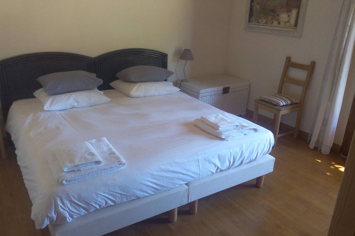 A neatly made bed with pillows, a bedside lamp, a wooden chair, and a small table.