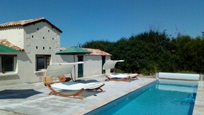 A poolside area with lounge chairs and umbrellas, a pool, and a building with a tiled roof. - Domaine Maison DoDo (Lamonzie-Saint-Martin)