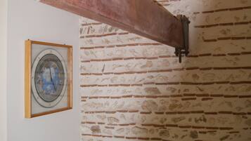 Une pièce aux murs en briques apparentes, avec une poutre en bois au plafond, un radiateur et une horloge encadrée accrochée au mur.