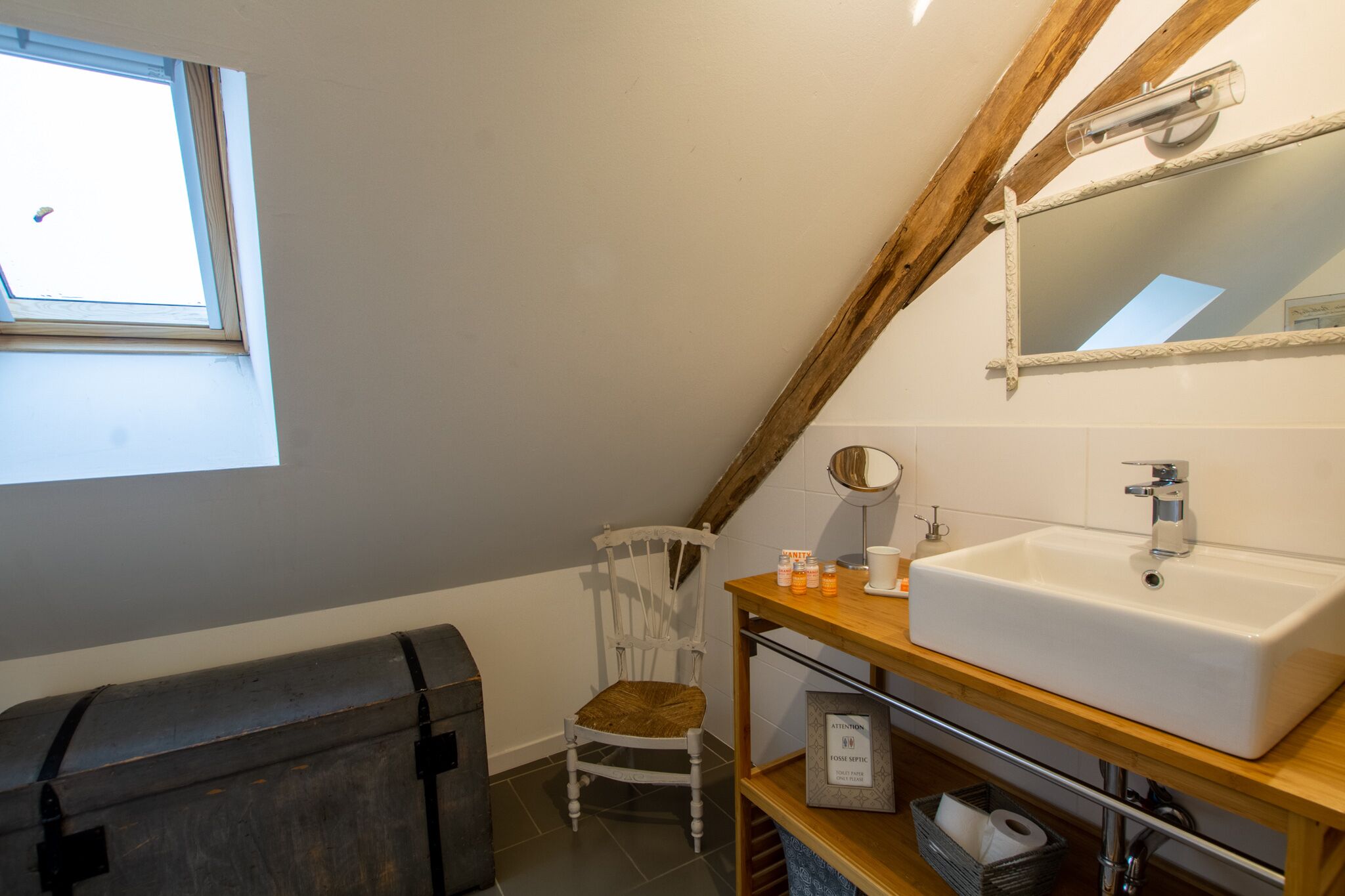 A bathroom with a large window, a white sink, a wooden chair, and a mirror.