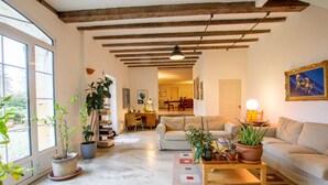 A spacious living room with a large window, a wooden ceiling, a sofa, a coffee table, and several potted plants. - Domaine Maison DoDo (Lamonzie-Saint-Martin)