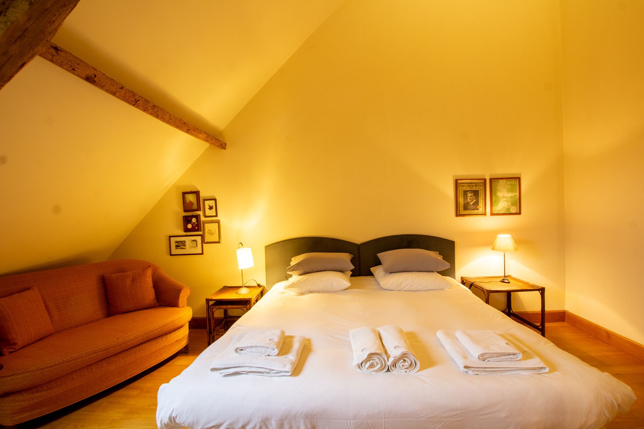 Una camera d'albergo con un letto, due comodini con lampade, un divano e quadri appesi al muro.