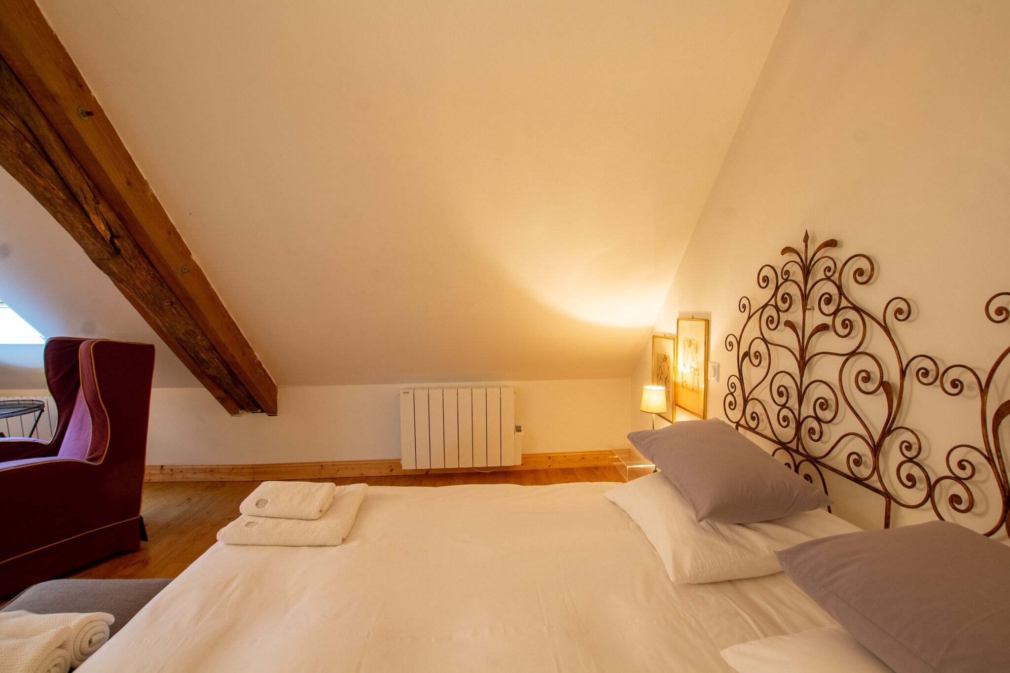 Un dormitorio con techo de madera, una cama con ropa blanca, una silla roja y un radiador.