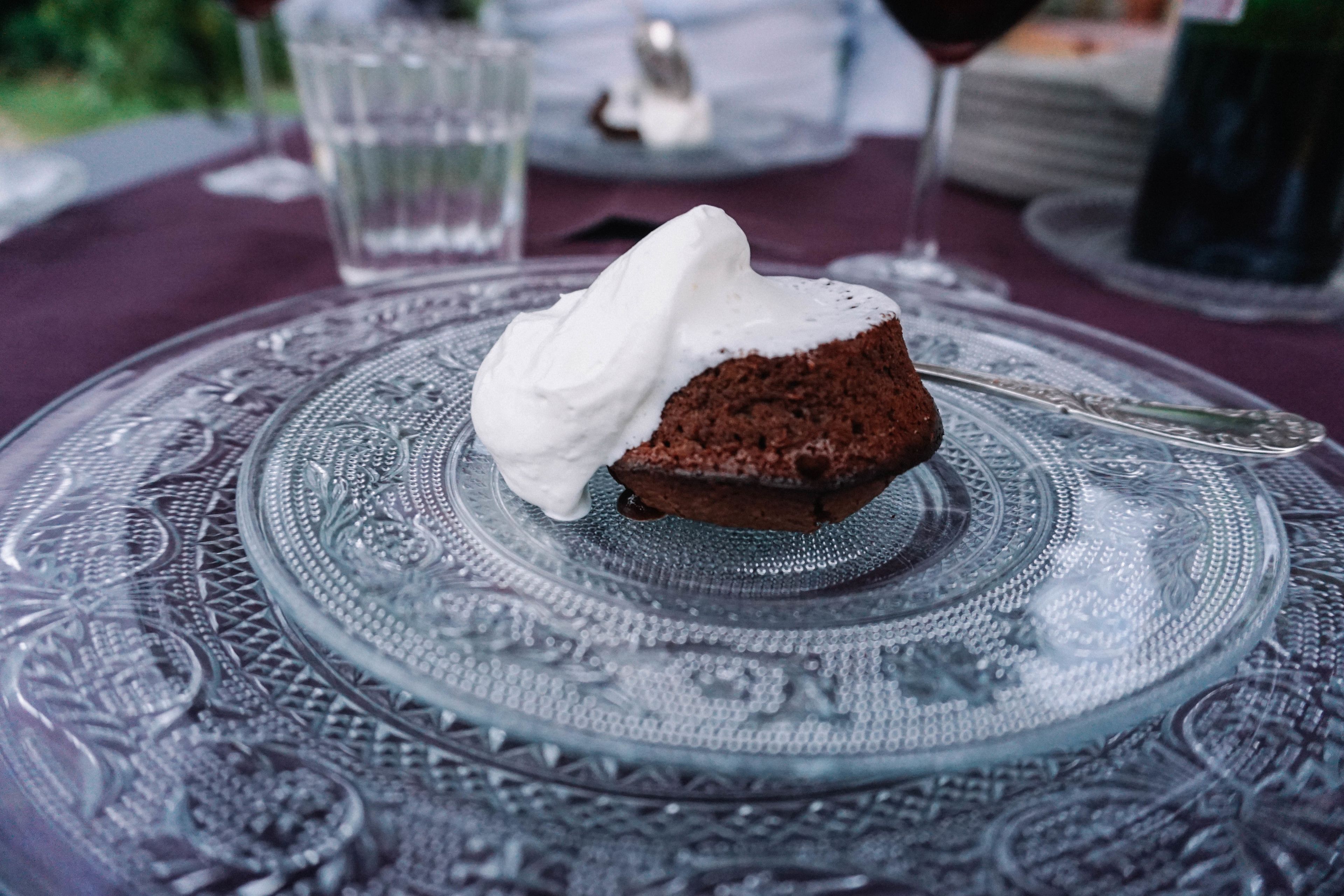 A dessert on a glass plate with intricate patterns, a glass of water, and a wine glass in the background.