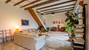 A spacious living room with a high ceiling, a staircase, a sofa, a coffee table, and a bookshelf filled with books. - Domaine Maison DoDo (Lamonzie-Saint-Martin)