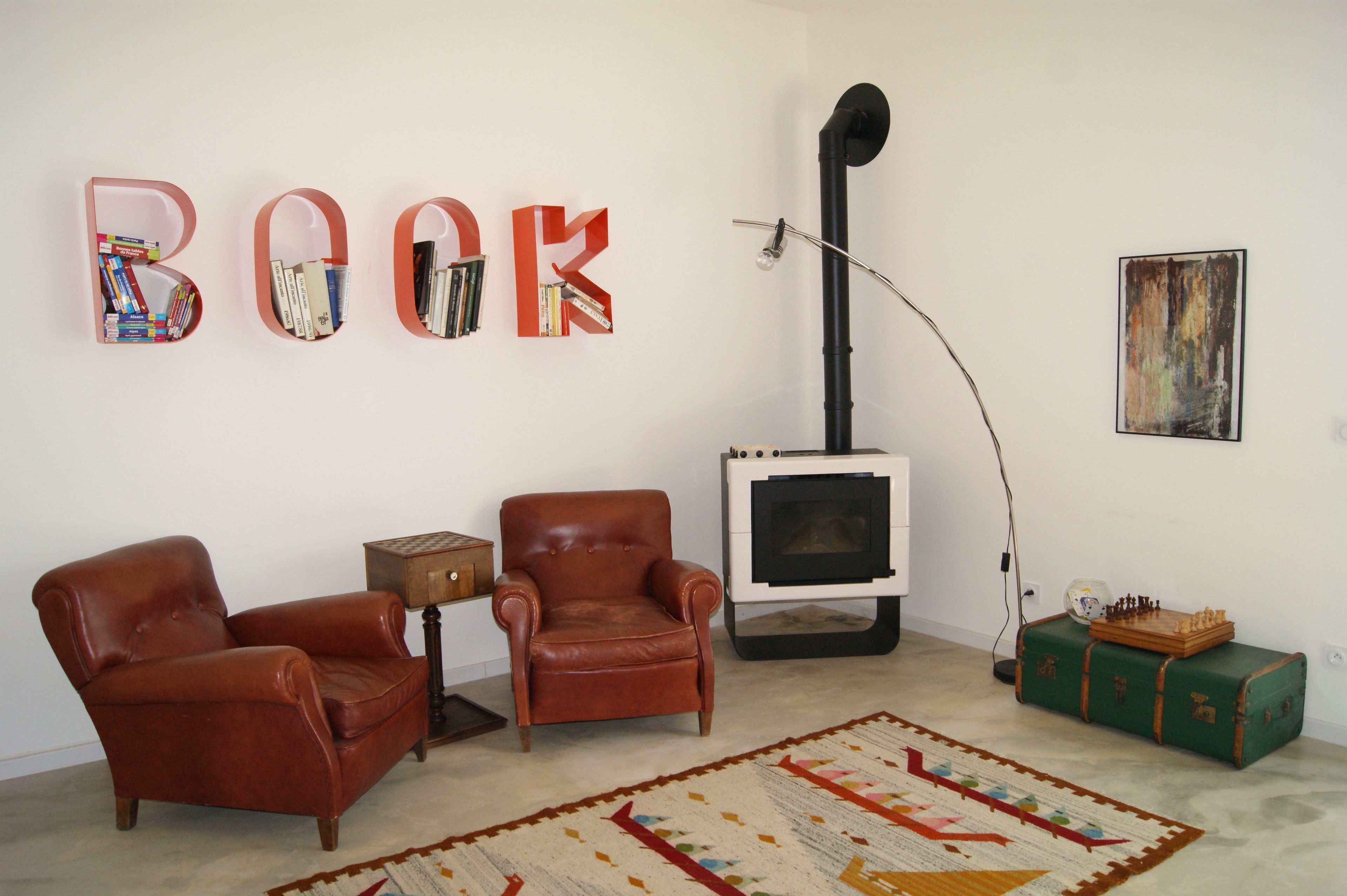 Un salón con dos sillones de cuero, una estantería llena de libros, una chimenea y un tablero de ajedrez sobre una maleta.