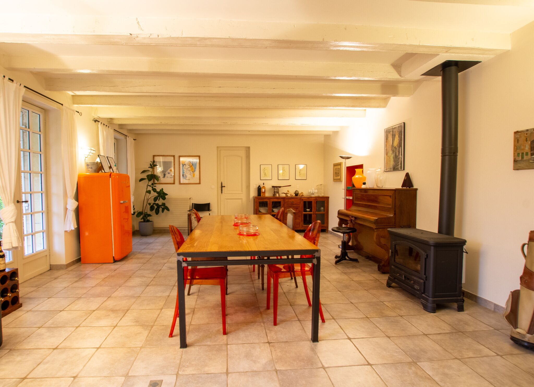 A dining area with a wooden table and red chairs, a kitchen with a stove, and a refrigerator.