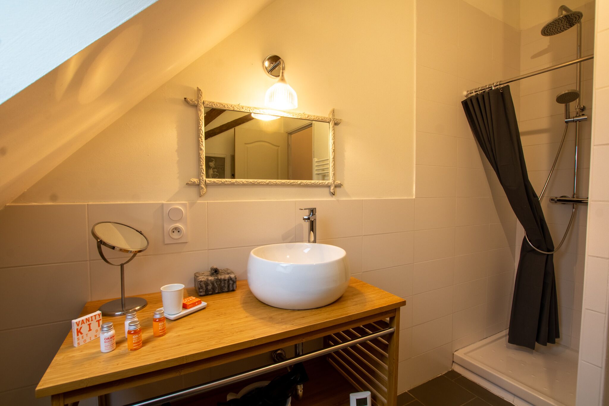 Een badkamer met een houten wastafelmeubel, een grote spiegel, een witte wasbak en een douche.