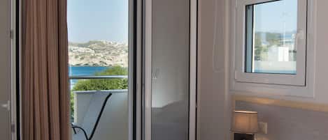 Habitación de hotel con cama, ventana con vista a la playa, puerta corrediza y una silla afuera.