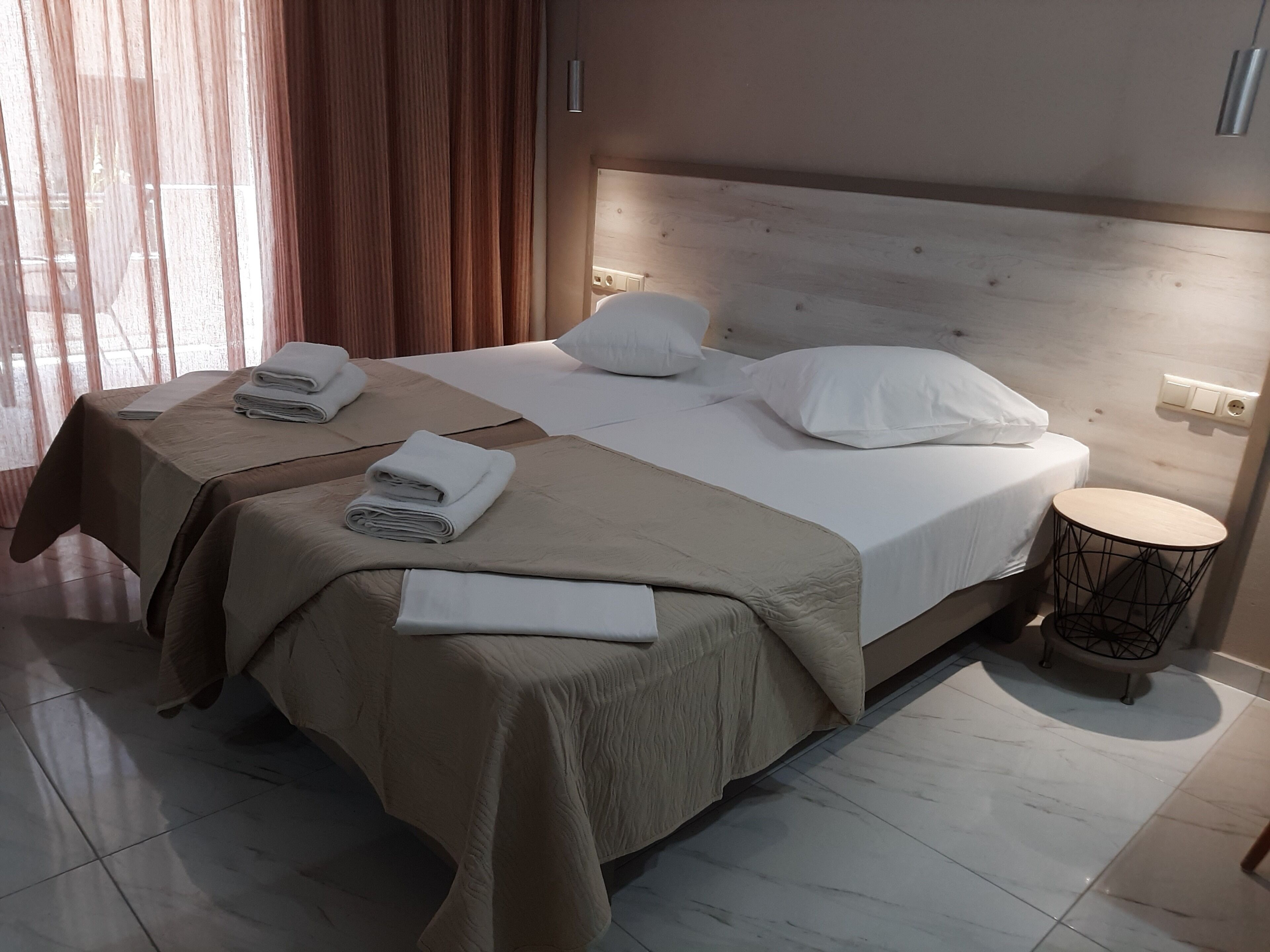 A hotel room with two beds, a round side table, and a large window with curtains.
