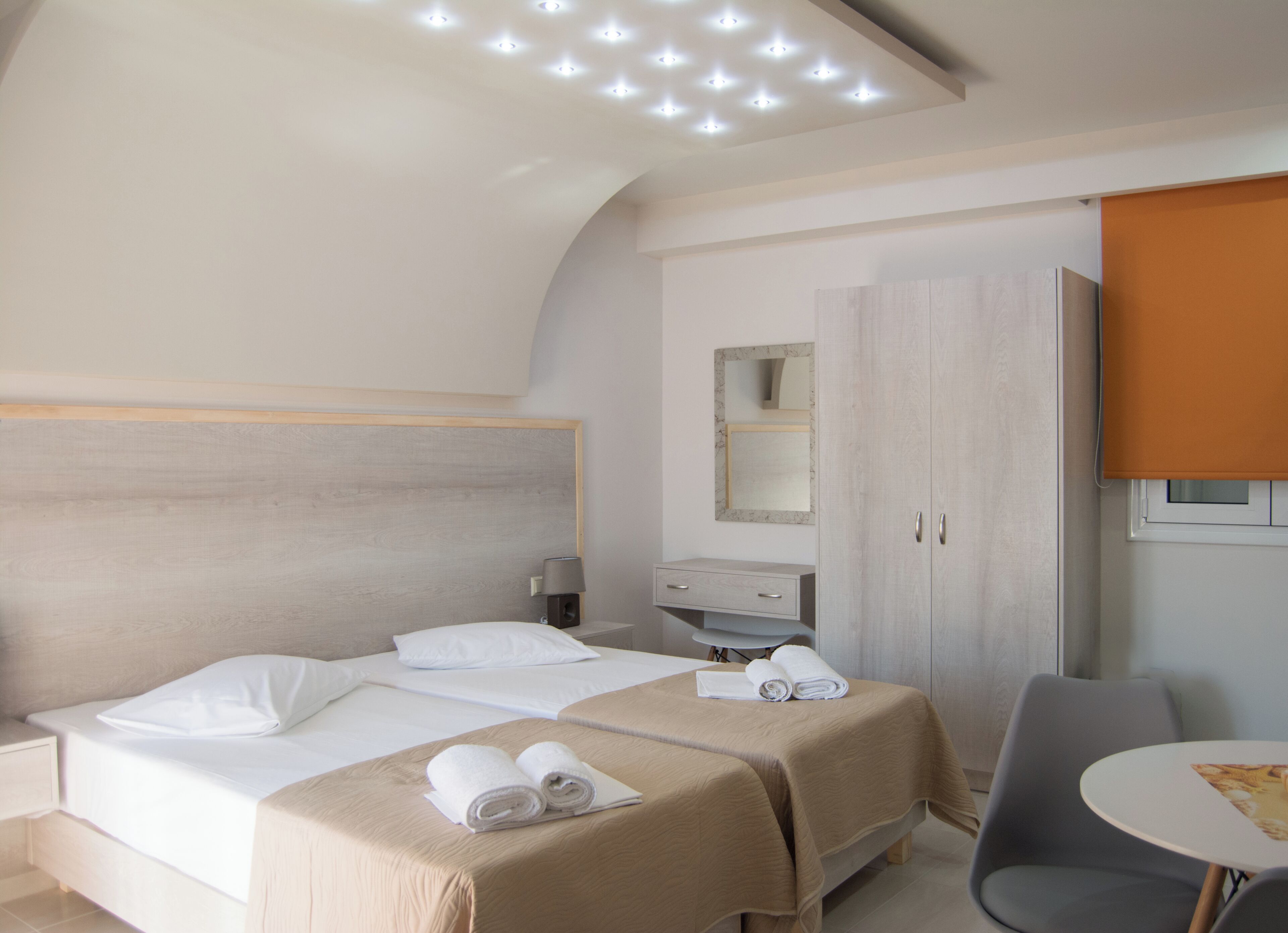 A hotel room with a bed, bedside tables, a desk, a chair, a mirror, and a wardrobe.