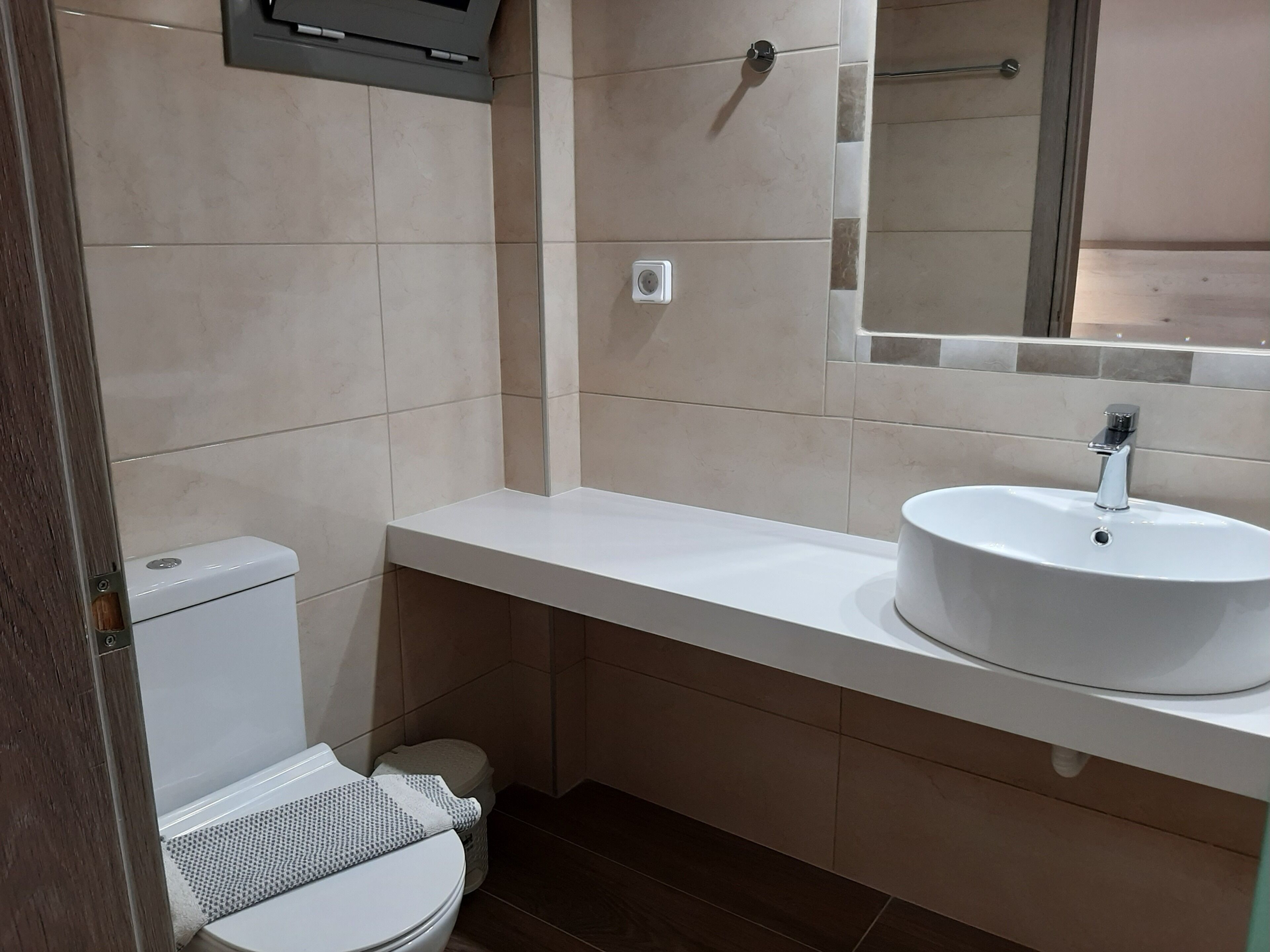 A bathroom with a toilet, sink, mirror, and tiled walls.