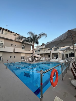 A swimming pool with a lifebuoy, lounge chairs, and a palm tree in a resort setting. - Sirena Apartments (Malevizi)