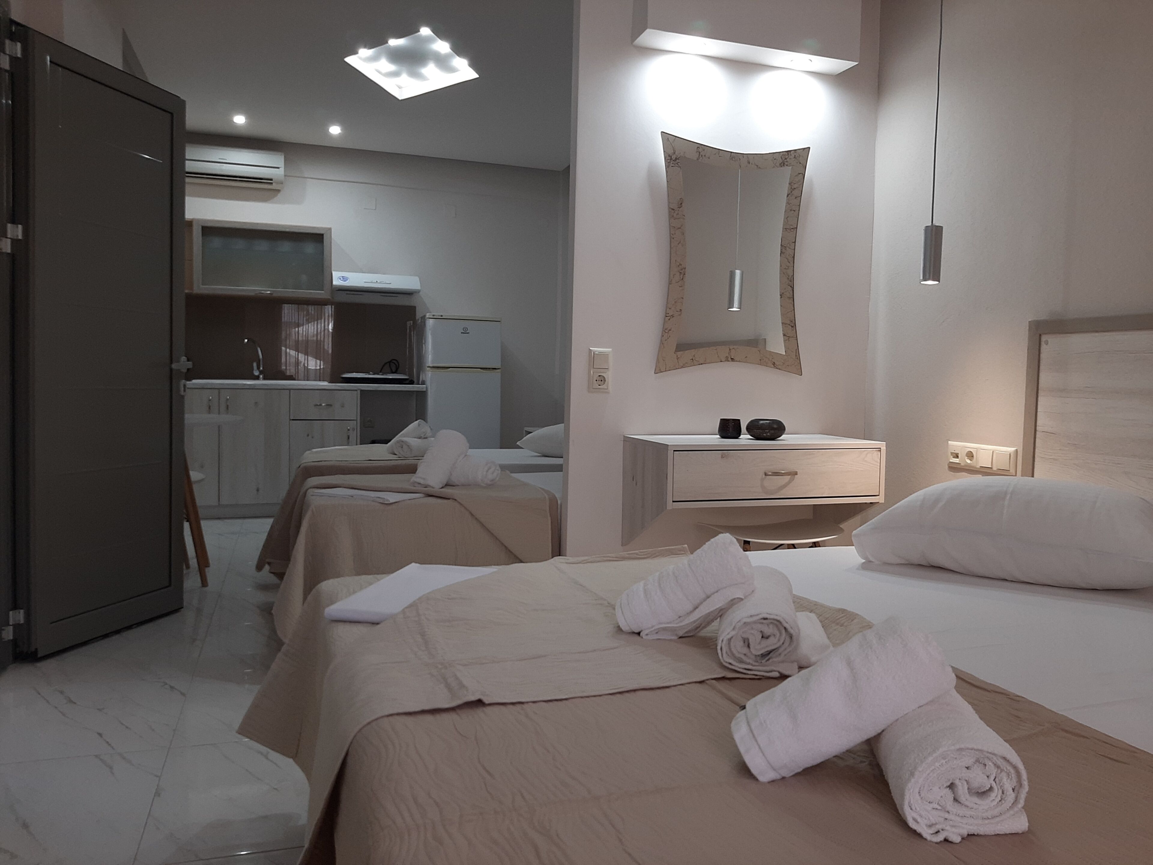 A hotel room with a bed, a bedside table, a mirror, and a kitchenette area.