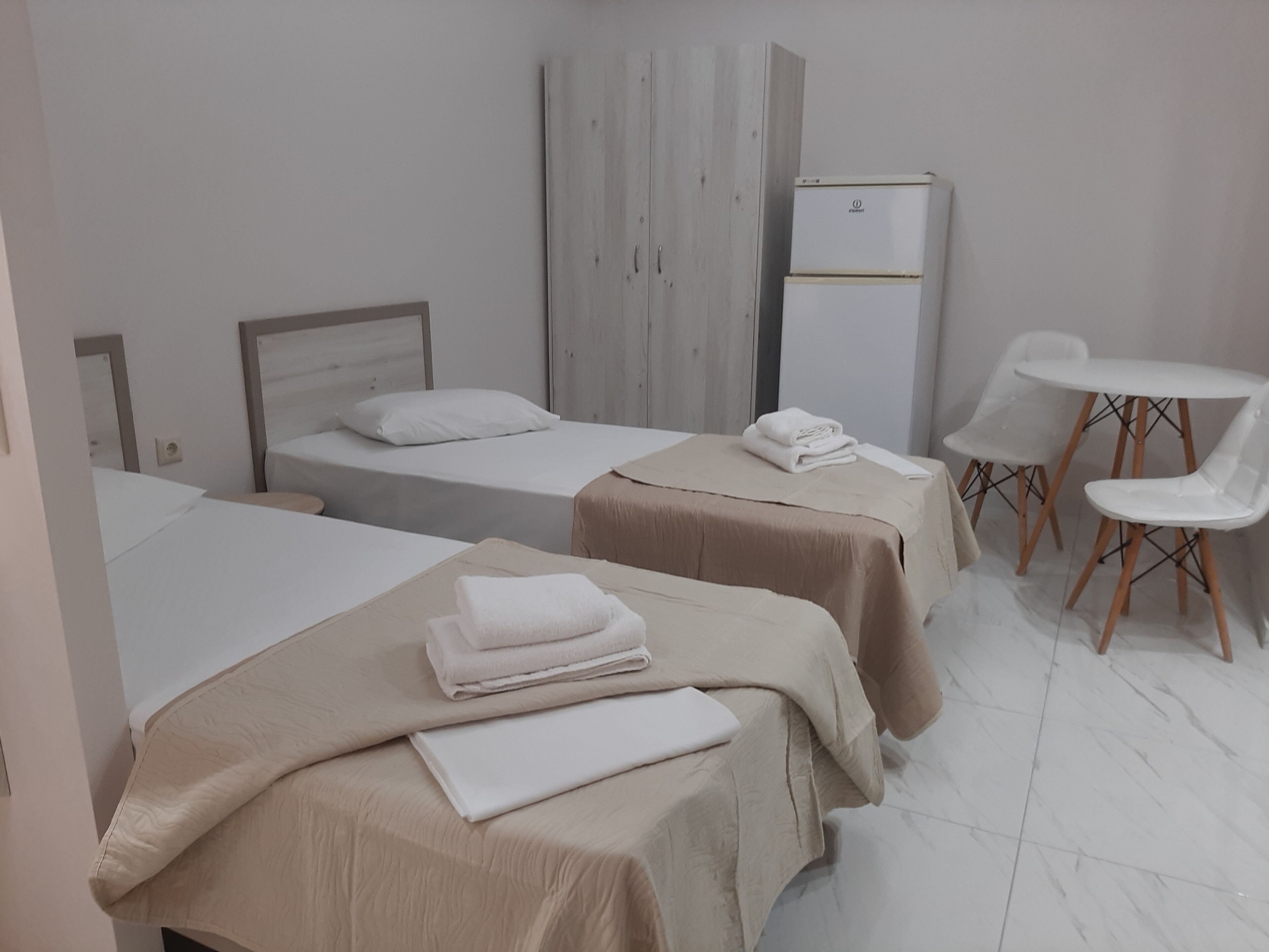 A hotel room with two beds, a small table, two chairs, and a refrigerator.