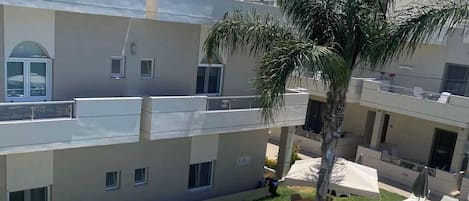 A multi-story building with a swimming pool, outdoor seating, and a palm tree.