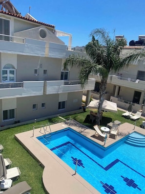 A multi-story building with a swimming pool, outdoor seating, and a palm tree.