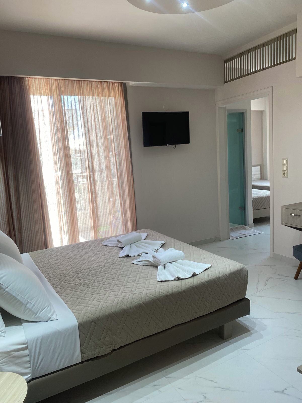 Ein Hotelzimmer mit einem Bett, einem flachbildfernseher an der Wand, einem sichtbaren Badezimmer durch eine offene Tür und einem kleinen Schreibtisch mit Stuhl.