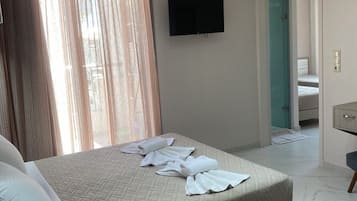 Quarto de hotel com uma cama, televisão de tela plana na parede, banheiro visível através de uma porta aberta e uma pequena mesa de trabalho com cadeira.