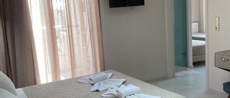 A hotel room with a bed, a flat-screen TV mounted on the wall, a bathroom visible through an open door, and a small desk with a chair.