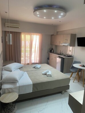 A modern hotel room with a bed, a small desk, a kitchenette, and a television. - Sirena Apartments (Malevizi)