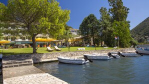 A marina with boats docked, a stone pathway, and a grassy area with umbrellas and lounge chairs. - Cleopatra Beach Hotel (Lefkada)
