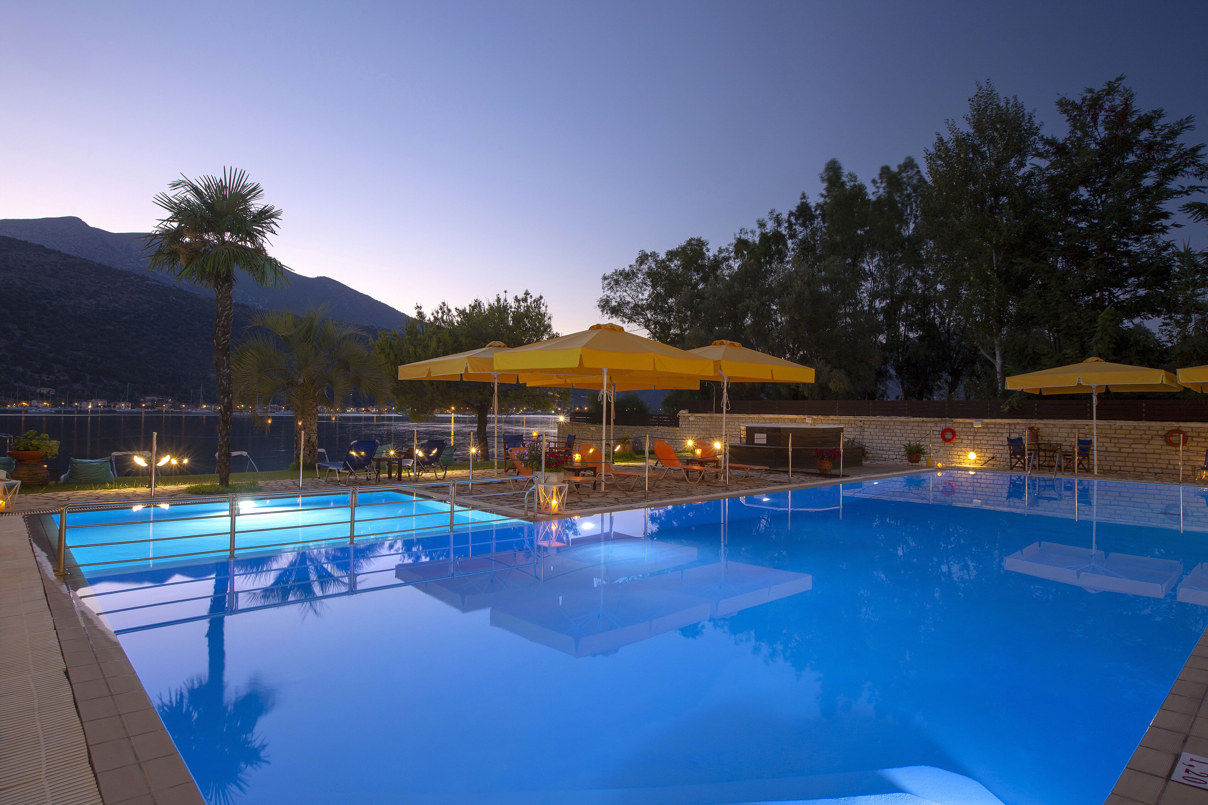 A swimming pool with multiple lanes, surrounded by lounge chairs and yellow umbrellas, with a mountain in the background.