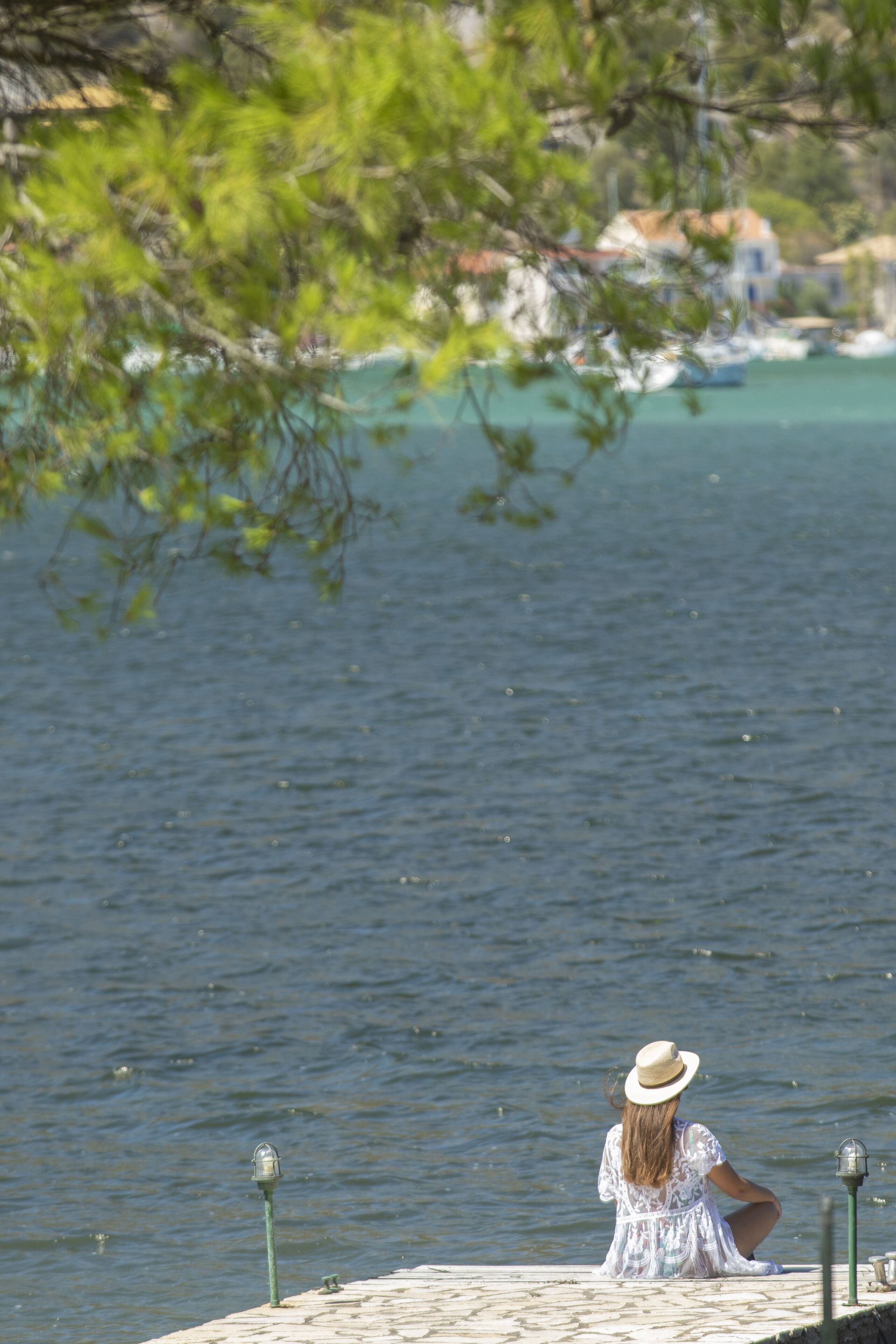 A woman sitting on a stone pier overlooking a body of water with buildings in the background.