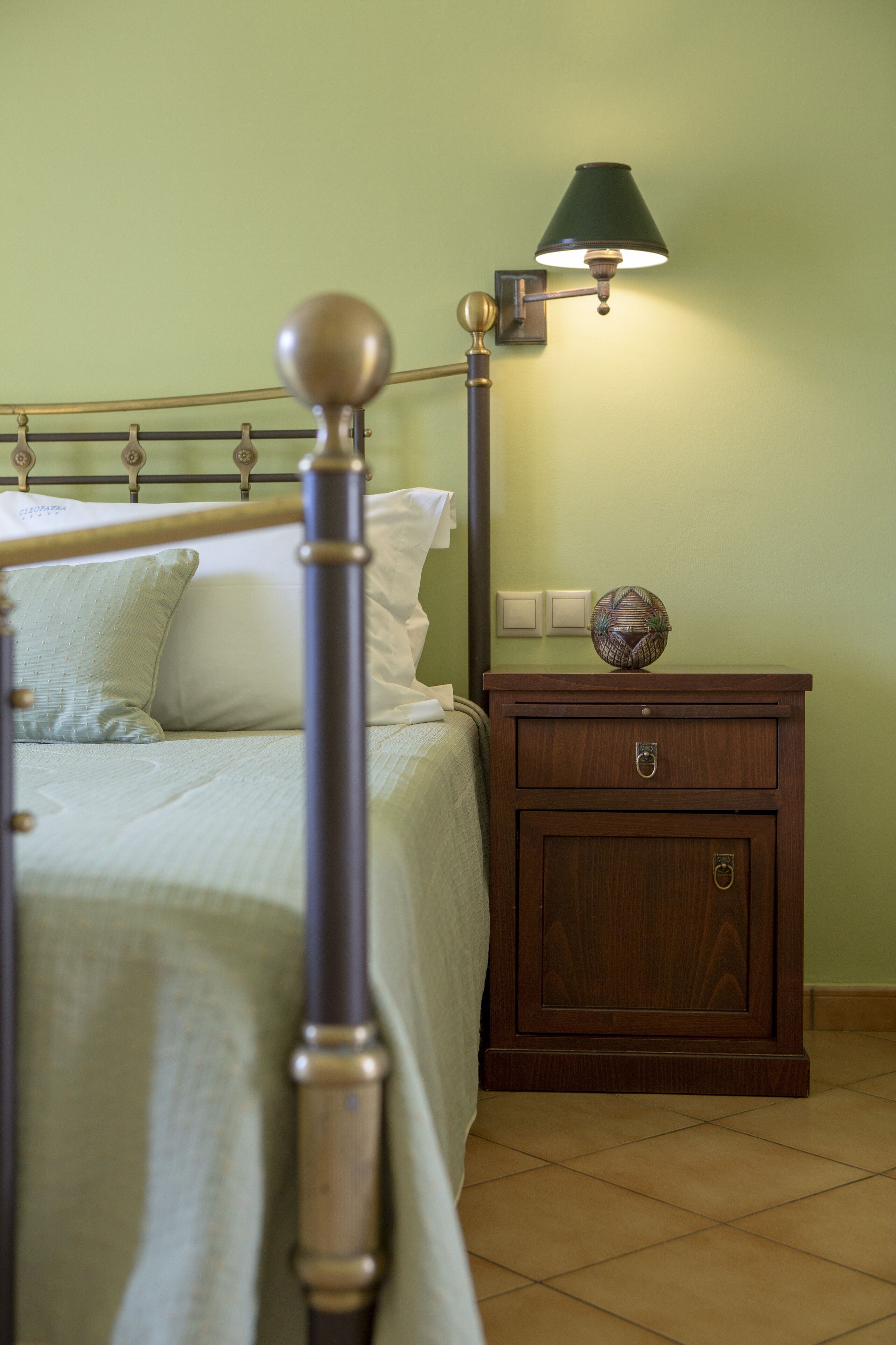 A bed with a metal headboard, a bedside table with a lamp, and a nightstand with a decorative item.